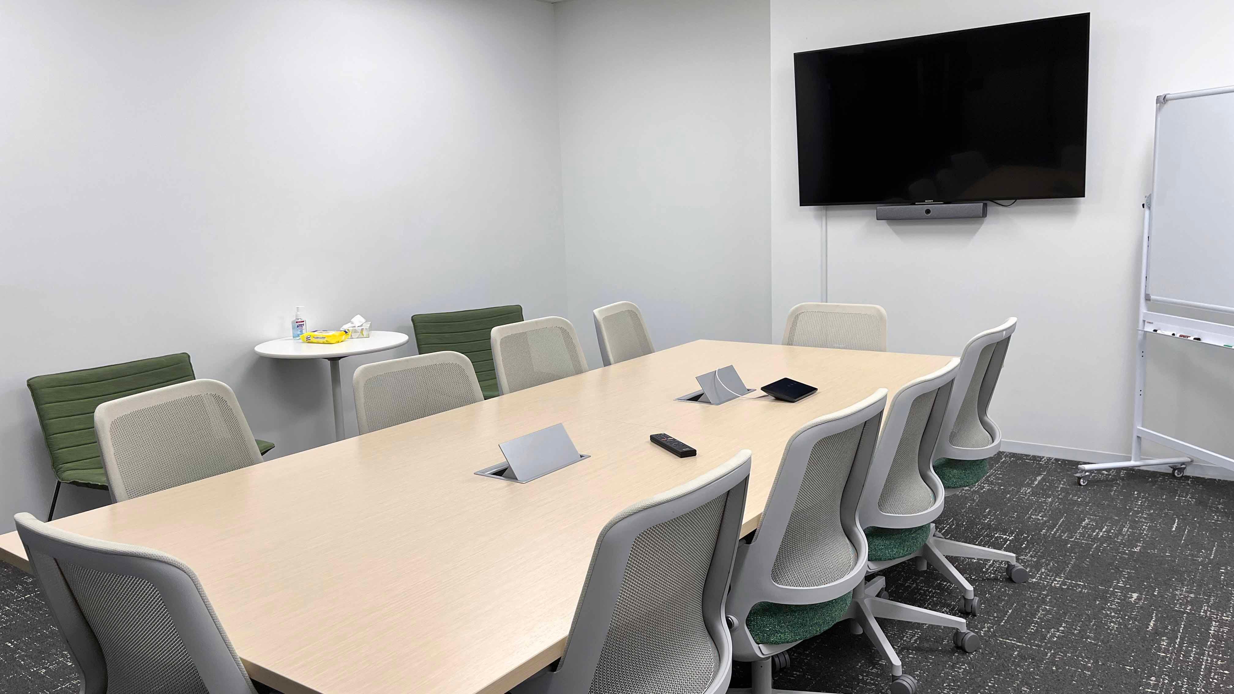 Image of room 104 of the USU Salt Lake Campus, showing a central table with 10 chairs, with a TV on the wall and a white board adjacent.