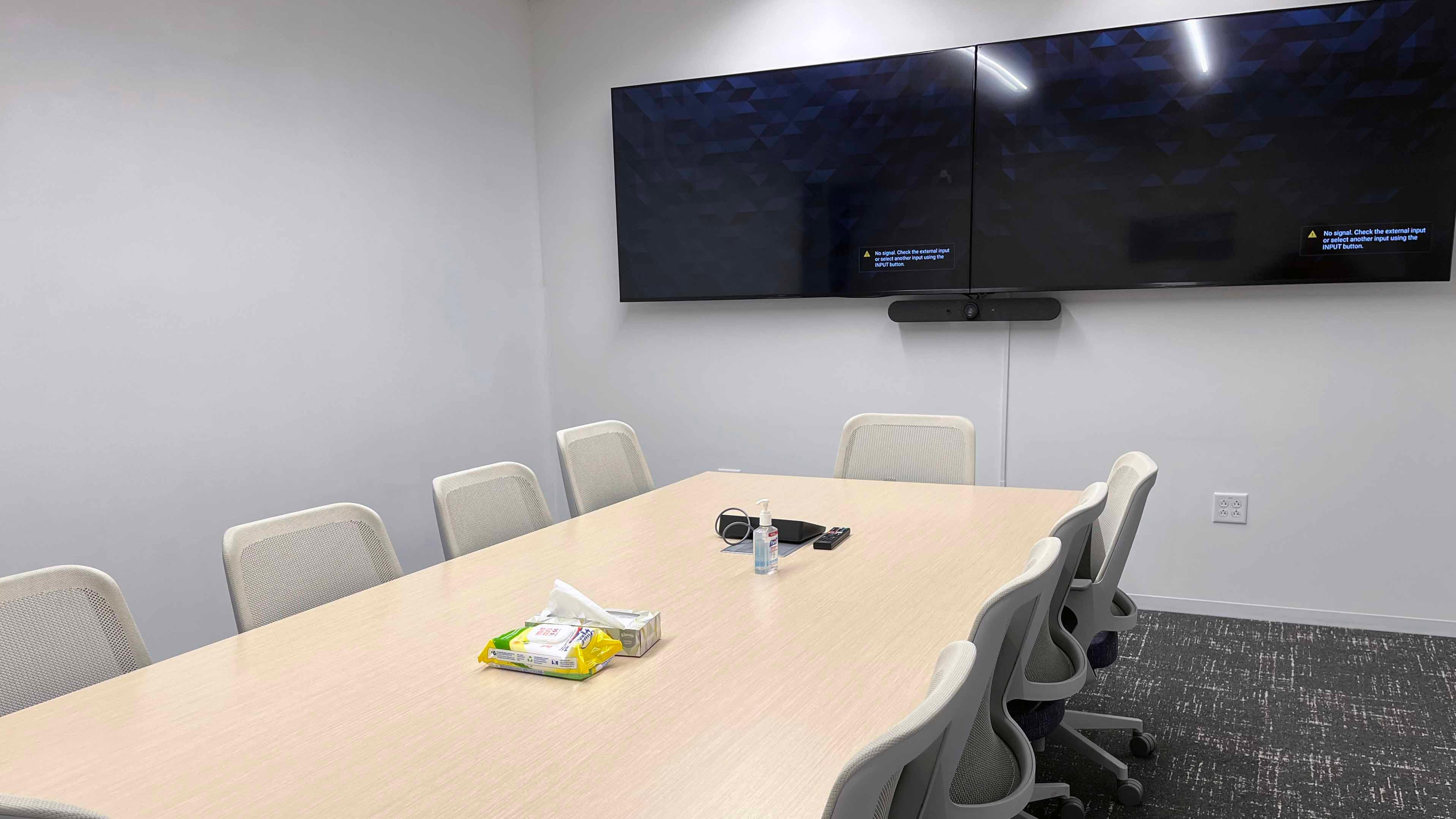 Image of room 112 inside the USU Salt Lake Campus showing a central conference table with 10 chairs and two TVs mounted on the wall.