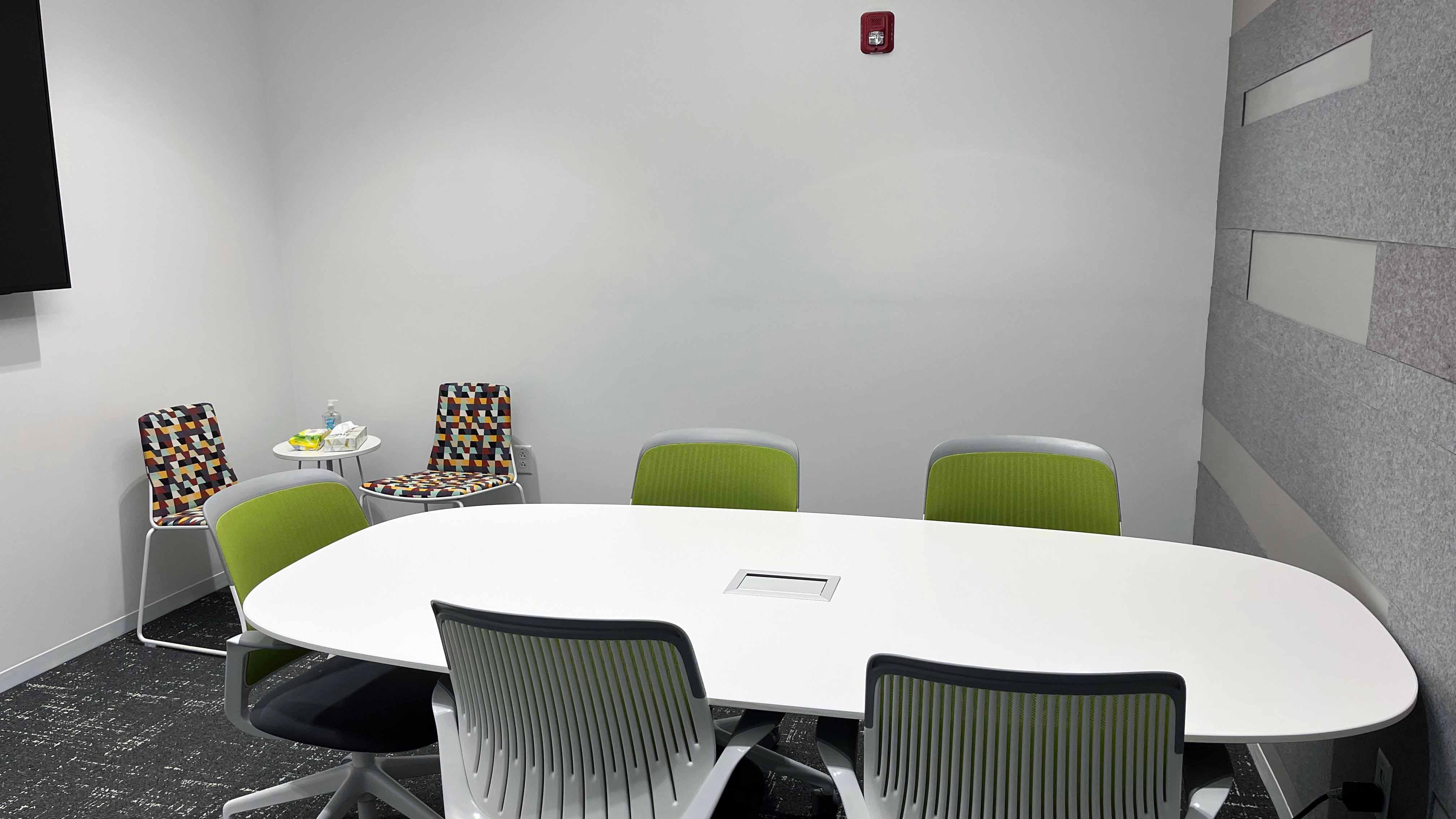 Image of room 106 inside the USU Salt Lake Campus, showing a central conference table surrounded by five chairs and two smaller chairs in the corner of the room.